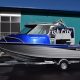 Black, grey, and blue boat wth a hard top canopy, black motor on trailer in front of fish city building