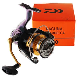Purple, orange, and back fishing reel, beside a orange box. The reel has a purple body, with a gold and black handle, and a silver line spool